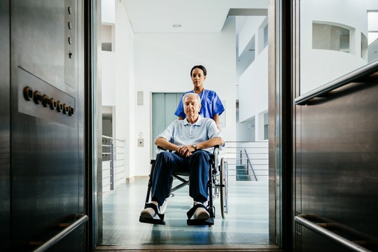 pielęgniarka wprowadzająca starszego mężczyznę na wózku do windy